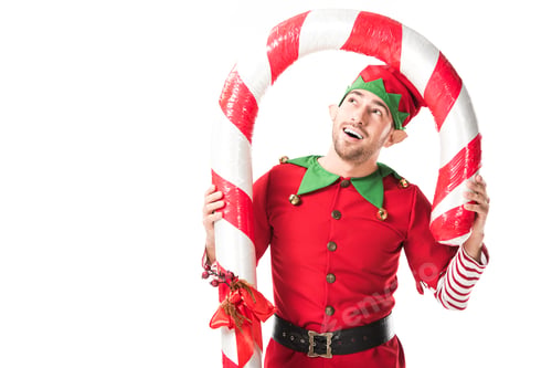 Preview: happy man in christmas elf costume standing under big candy cane isolated on white