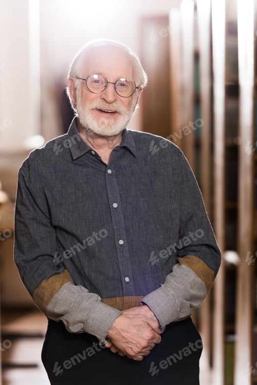 Preview: happy grey hair librarian standing between shelves