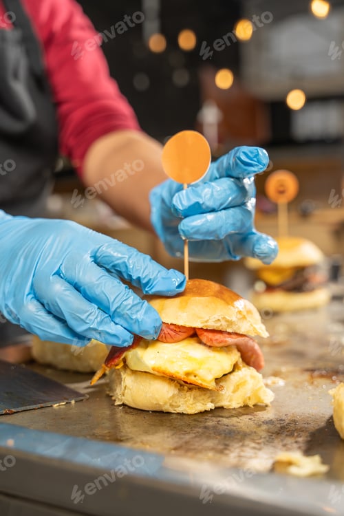 Preview: Cook wearing blue gloves preparing delicious burger in a fast food restaurant