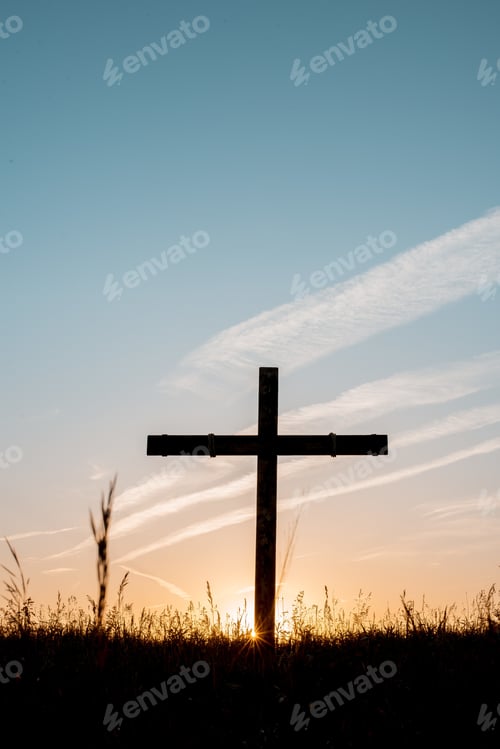 Preview: Silhouette of wooden cross in a grassy field with a blue sky in the background in a vertical shot