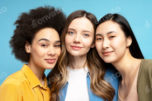 Preview: Portrait of attractive women of different ethnicities smiling together on blue background