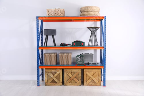 Preview: Metal shelving unit with wooden crates and different household stuff near light wall indoors