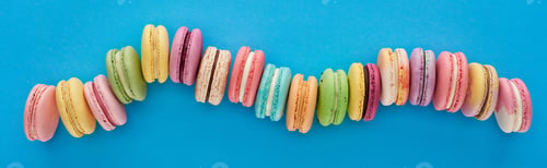 Preview: top view of multicolored delicious French macaroons in curved line on blue bright background,