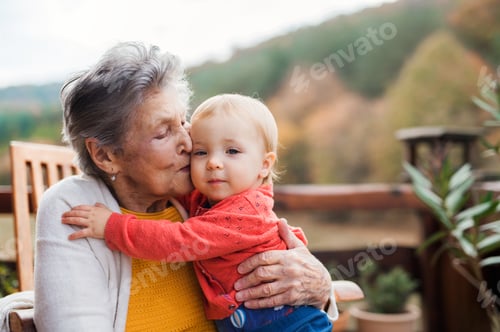 Preview: Elderly woman kissing a toddler great-grandchild on a terrace in autumn.