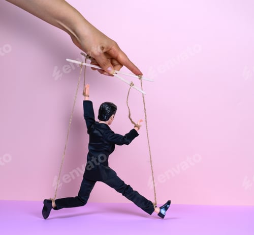 Preview: female hand with a puppet of a man in a black business suit on a pink background