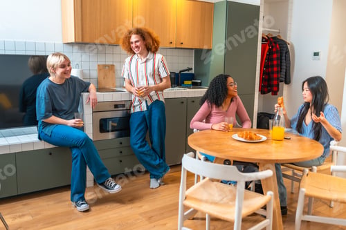 Preview: Cheerful diverse friends enjoying breakfast and talking together in modern kitchen