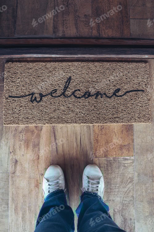 Preview: High angle view of welcome mat in door over wooden floor with woman foot-ware near of it