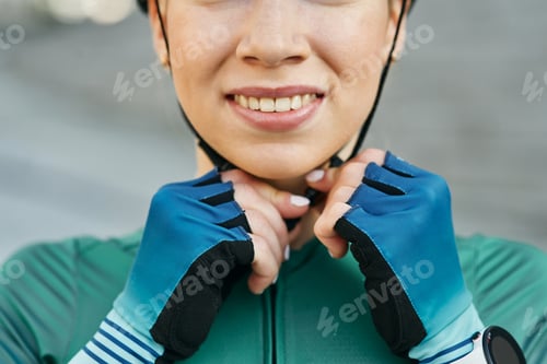 Preview: Cropped portrait of young woman, female cyclist smiling and fastening her cycling helmet while