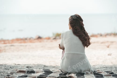 Preview: rear view of woman resting on blanket alone on sandy beach