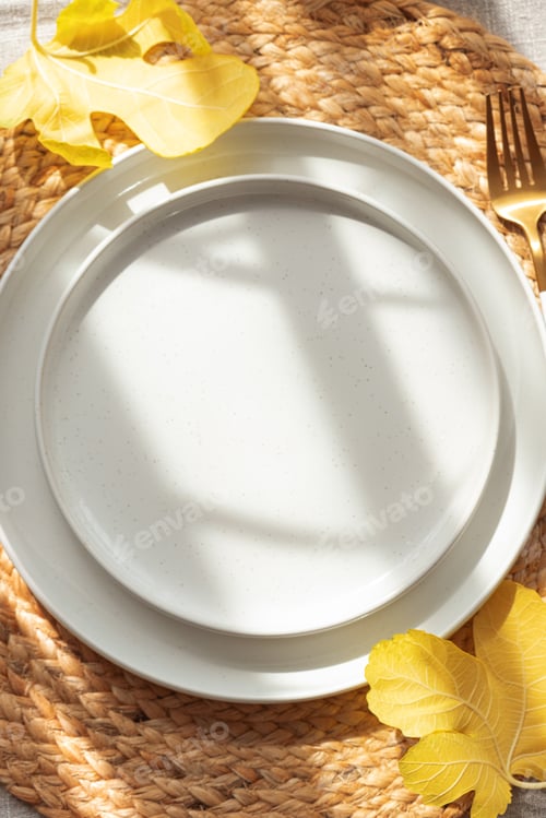 Preview: Table Setting with Yellow Leaves on White Plate and Woven Placemat under Sun Light
