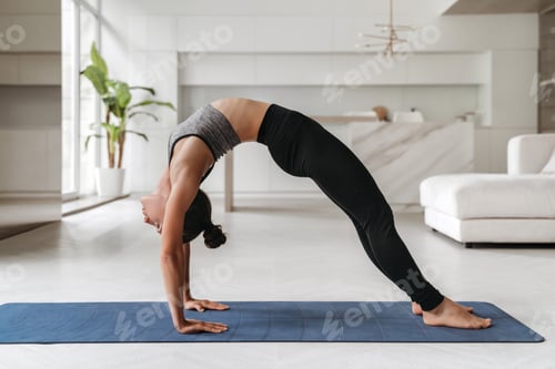 Preview: Young sporty woman practicing yoga at home on mat in Bridge pose