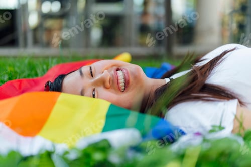 Preview: Happy woman lying on the grass with a lgbt flag