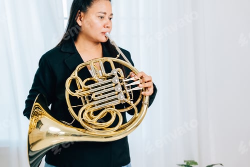 Preview: Dressed in black, a woman blows a gleaming French horn in gold