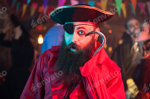 Preview: Portrait of funny man in a pirate costume playing with his hand hook at halloween celebration