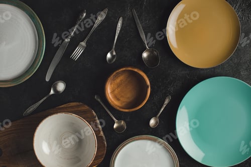 Preview: flat lay with arranged ceramic plates, antique silverware and cutting board isolated on black