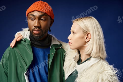Preview: young woman embracing african american man in winter attire of blue backdrop, diverse couple