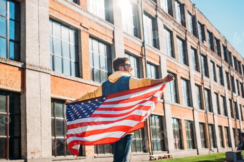 Preview: Back View of Young Man With American Flag in Hands on Street