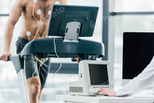 Preview: cropped view of doctor conducting endurance test with sportsman in gym