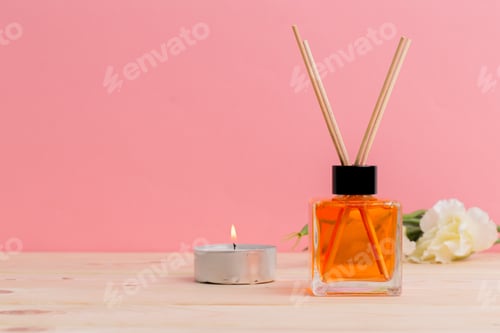 Preview: Decorative diffuser with fragrance beside a candle on a wooden table against a pink background