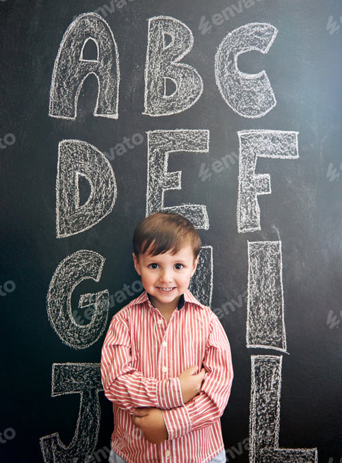 Preview: Portrait of an adorable little boy standing in front of a blackboard with letters written on it