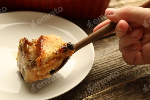 Preview: Woman eating tasty bread pudding at wooden table, closeup