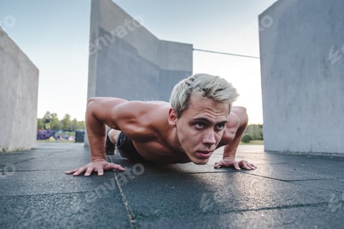 Preview: Young athletic man doing push ups on parkour area. Training alone outdoors.