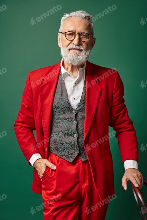 Preview: handsome man dressed as Santa with glasses and hand on backrest looking at camera, winter concept