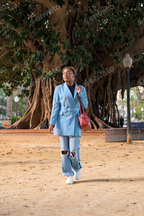 Preview: Black businesswoman with a blue suit cross a park of a city
