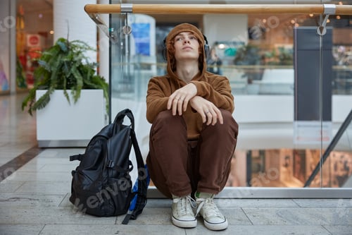 Preview: Upset teenage boy in headphones sitting nearby moving staircase