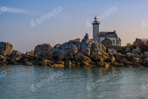 Preview: White lighthouse near rock formations on the shore of the sea under the beautiful sky