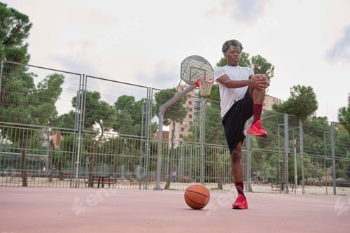Preview: young African-American basketball player stretching his legs before playing