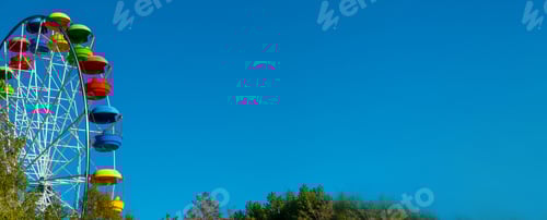 Preview: landscape of an amusement park with the top of a Ferris wheel showing above the tree tops against a