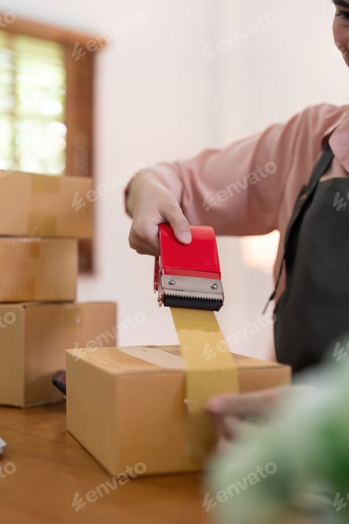Preview: Woman use scotch tape to attach parcel boxes to prepare goods for the process of packaging