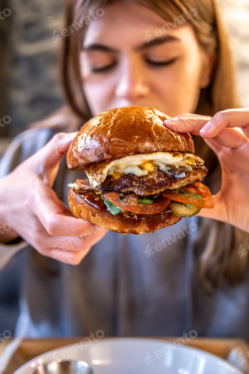 Preview: Big appetizing burger with meat in female hands in a cafe.