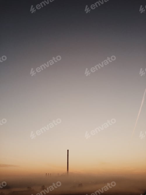 Preview: Factory On Foggy Field Against Sky During Sunrise