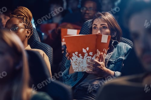 Preview: Scared woman watching horror film at movie theatre.