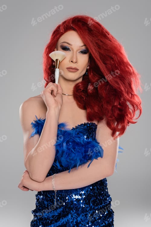 Preview: Portrait of drag queen in wig and dress holding makeup brush isolated on grey