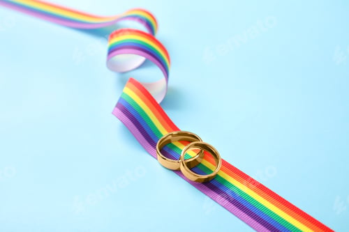 Preview: Wedding rings and rainbow ribbon on color background. Gay symbol
