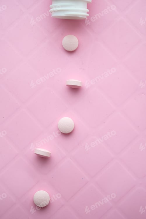 Preview: A collection of scattered white tablets is placed on a soft pink surface for contrast