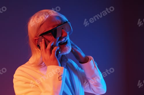Preview: Stylish senior man with glasses, smiling while talking on the phone against a colorful background