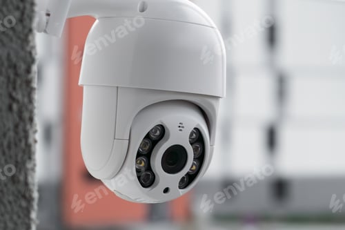 Preview: Modern CCTV camera on a wall with a blurred multi-storey building on the background.
