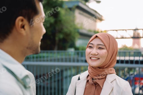 Preview: Muslim businesswoman smiling at colleague outdoors in urban setting