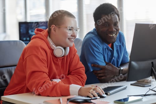 Preview: Two happy young intercultural cyber security engineers sitting by workplace