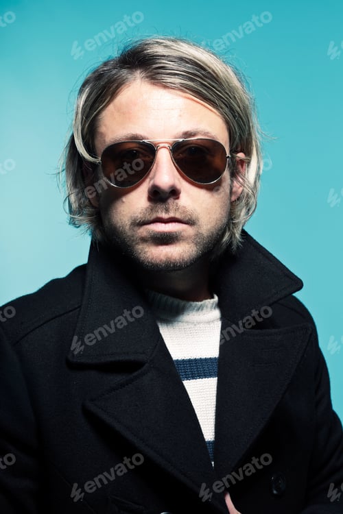 Preview: Studio Portrait Of Young Casual Man With Long Blond Hair Wearing Sunglasses And Black Jacket. Blue