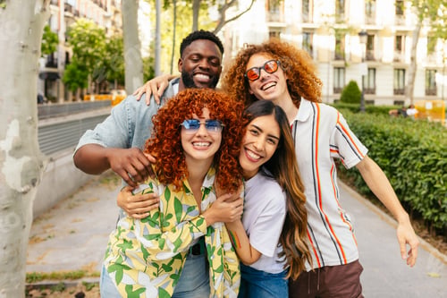 Preview: Portrait of happy multi ethnic friends embracing in the city park