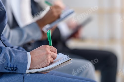 Preview: People with notepads listening to presentation in modern office
