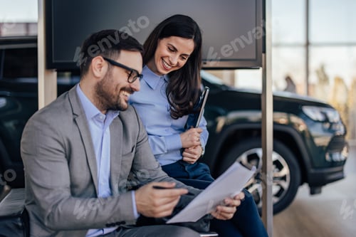 Preview: Smiling caucasian man with glasses, pointing out mistakes in document to his female colleague.