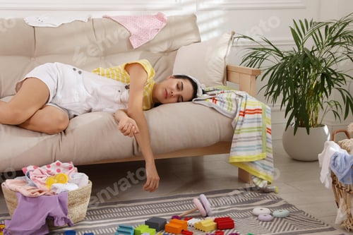 Preview: Tired young mother sleeping on sofa in messy living room