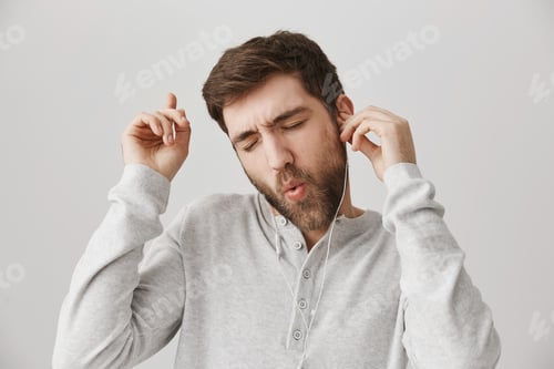 Preview: Close-up portrait of happy positive young male with beard, dancing and listening music in earphones