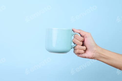Hand Holding Blue Mug Against Blue Background
